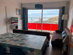 a living room with a table and a large window at LES BALCONS ROUGES - VUE MER in Sainte-Cécile-Plage