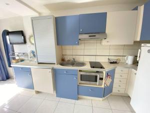 eine Küche mit blauen Schränken, einer Spüle und einer Mikrowelle in der Unterkunft Studio 106, Port Vénus au village naturiste in Cap d'Agde