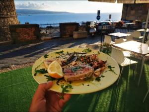 una persona che tiene in mano un piatto di pesce con un limone di Murat Guesthouse a Pizzo