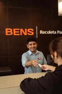 a man sitting at a desk with a woman holding a cell phone at BENS - Recoleta Park in Buenos Aires