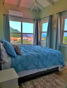 a bedroom with a bed with blue sheets and windows at La Pelle in Soufrière