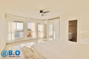 a white bedroom with a bed and windows at על הים in Netanya