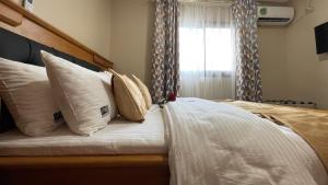 a bedroom with a bed with white pillows and a window at JPN SQUARE Douala in Douala