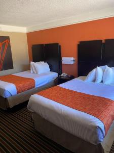 2 camas en una habitación de hotel con paredes de color naranja en Howard Johnson by Wyndham Historic Lake Charles, en Lake Charles