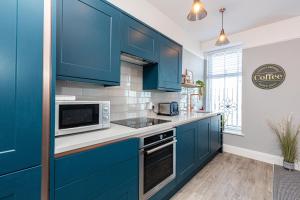 a kitchen with blue cabinets and a microwave at Stylish Seafront Apartment - Sleeps 6 - Gateway to the Lakes in Morecambe