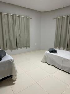 two beds in a white room with curtains at Apto apoio Serra da Capivara in São Raimundo Nonato