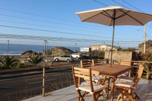 een houten tafel en stoelen met een parasol en de oceaan bij Puesta del Sol in Pelluhue
