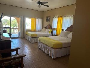 two beds in a hotel room with yellow curtains at Brytan Villa in Treasure Beach