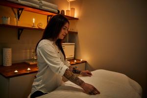 Una donna con un tatuaggio sul braccio seduta su un letto di The Nunnery and Spa a Leura