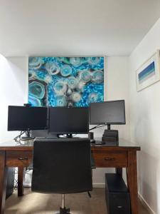 a desk with two monitors and a painting on the wall at Boxwood IXL Lux Hobart Waterfront in Hobart
