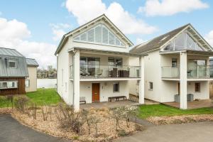 a white house with a porch and a balcony at Lakeside property with spa on a nature reserve Bryony HM35 in Somerford Keynes