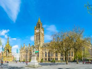a large building with a clock tower in front of it at Pass the Keys 5 Min Walk Free Parking Coop Live and Ethiad Arena in Manchester