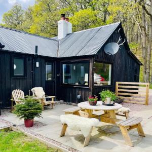 a black cabin with a picnic table and benches at Stags Hide - Aviemore 