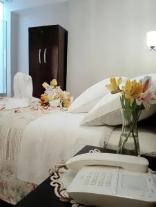 Una cama blanca con teléfono y un jarrón de flores. en HOTEL CASA REAL, en Tacna