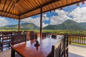 un restaurante con mesa, sillas y montañas en Teras Sawah Guest House Syariah, en Sembalun Lawang