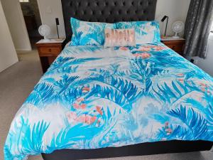 a bed with a blue comforter with tropical plants at Kerikeri Sunny Modern 2 Bedroom Apartment in Kerikeri