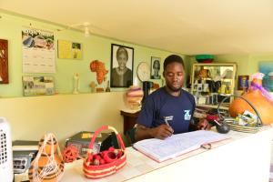 un homme assis à un comptoir qui signe un livre dans l'établissement Zion Camp, à Entebbe