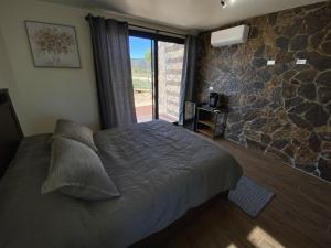 - une chambre avec un lit et un mur en pierre dans l'établissement Estancia Cataviña Valle de Guadalupe, à Valle de Guadalupe