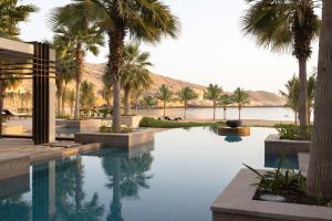 uma piscina com palmeiras e um corpo de água em Jumeirah Muscat Bay em Mascate