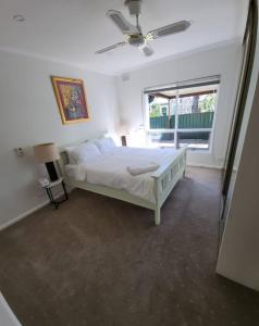 a white bedroom with a bed and a window at Beautiful and cozy home in Glenunga