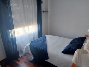 Un dormitorio con una cama con almohadas azules y una ventana en Piso Loredo, en Loredo