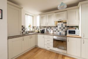 a white kitchen with white cabinets and a microwave at Beautiful City Center Apartment with a River View - Free Parking! in Belfast