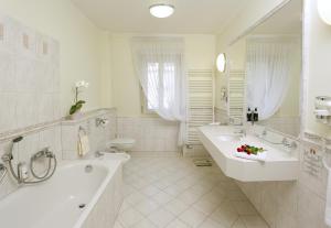 uma casa de banho com 2 lavatórios, uma banheira e um WC. em Hotel Mignon em Karlovy Vary