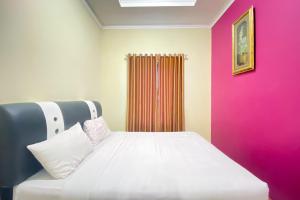 1 dormitorio con cama blanca y pared rosa en RedDoorz Syariah at D'Rizs Homestay en Bukittinggi