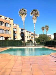 una piscina con palme di fronte a un edificio di Appartement avec piscine proche de la mer a La Londe-les-Maures