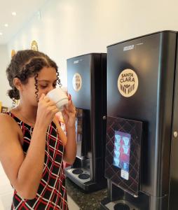uma jovem a beber de uma chávena em frente a uma máquina de café em Pousada Concha Dourada em Maragogi