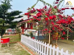 una valla blanca con un árbol con flores rojas en Sunny Villa Cottage en Sivasagar