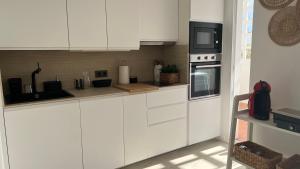 una cucina con mobili bianchi e un forno a microonde di Playa y Comodidad en Benicàssim a Benicàssim