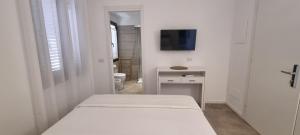 a white bedroom with a bed and a desk and a tv at Anthias Rooms Affittacamere in Porto San Paolo