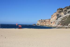 a sandy beach next to the ocean with cliffs at The Green Gate Patio House in Nazaré