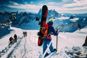 un homme tenant un snowboard au sommet d'une montagne dans l'établissement La Ferme à Roland ski in - ski out - Happy Rentals, à Chamonix-Mont-Blanc