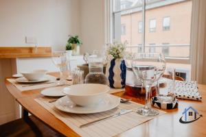 a wooden table with plates and wine glasses on it at Contemporary flat, sleeps 4, very central, parking in Northampton