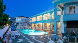a large blue building with a pool and tables and chairs at Anna's Studios & Apartments in Laganas