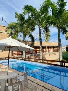 a pool with palm trees and a table and an umbrella at POUSADA TAIEIRAS in Maragogi