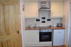 Mc Courts Barn, Tiny house in the Mournes في Hilltown: مطبخ بدولاب بيضاء ومغسلة وموقد