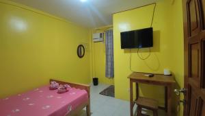 Habitación con mesa rosa y TV en una pared amarilla. en R & R (Rest & Relax) Guesthouse en Siquijor