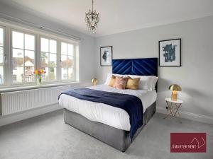 a bedroom with a large bed with a blue headboard at Thames Ditton - Luxury 4 Bedroom House - Garden and Parking in Thames Ditton