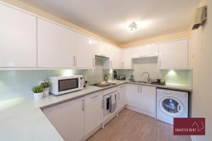 eine Küche mit weißen Schränken, einer Waschmaschine und einem Trockner in der Unterkunft Maidenhead - 2 Bed & parking in Maidenhead