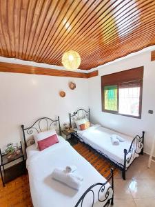 two beds in a bedroom with a wooden ceiling at Olympe Surf & Yoga in Tamraght Ouzdar