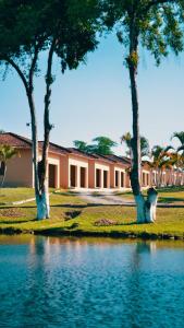 a building with three trees next to a body of water at O Paturi - Village Hotel in Guaratinguetá