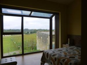 a bedroom with a large window looking out at a field at 4 bedrooms house with private pool jacuzzi and wifi at Roxos in Santiago de Compostela