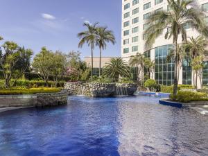 a pool in front of a building with palm trees at Aparta Hotel Torres de Suites in Quito