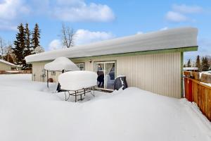 a house covered in snow with a table and a chair at Friendly Cove in Anchorage