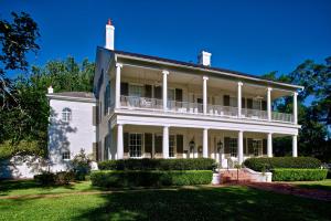 a large white house with a porch and bushes at Ravenna Bed and Breakfast in Natchez