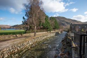 a river with a stone wall next to a building at The Ullswater Inn- The Inn Collection Group in Glenridding