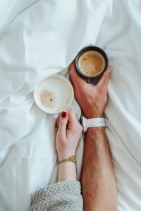 a person laying in bed holding a cup of coffee at Hotel Janssen in Valkenburg